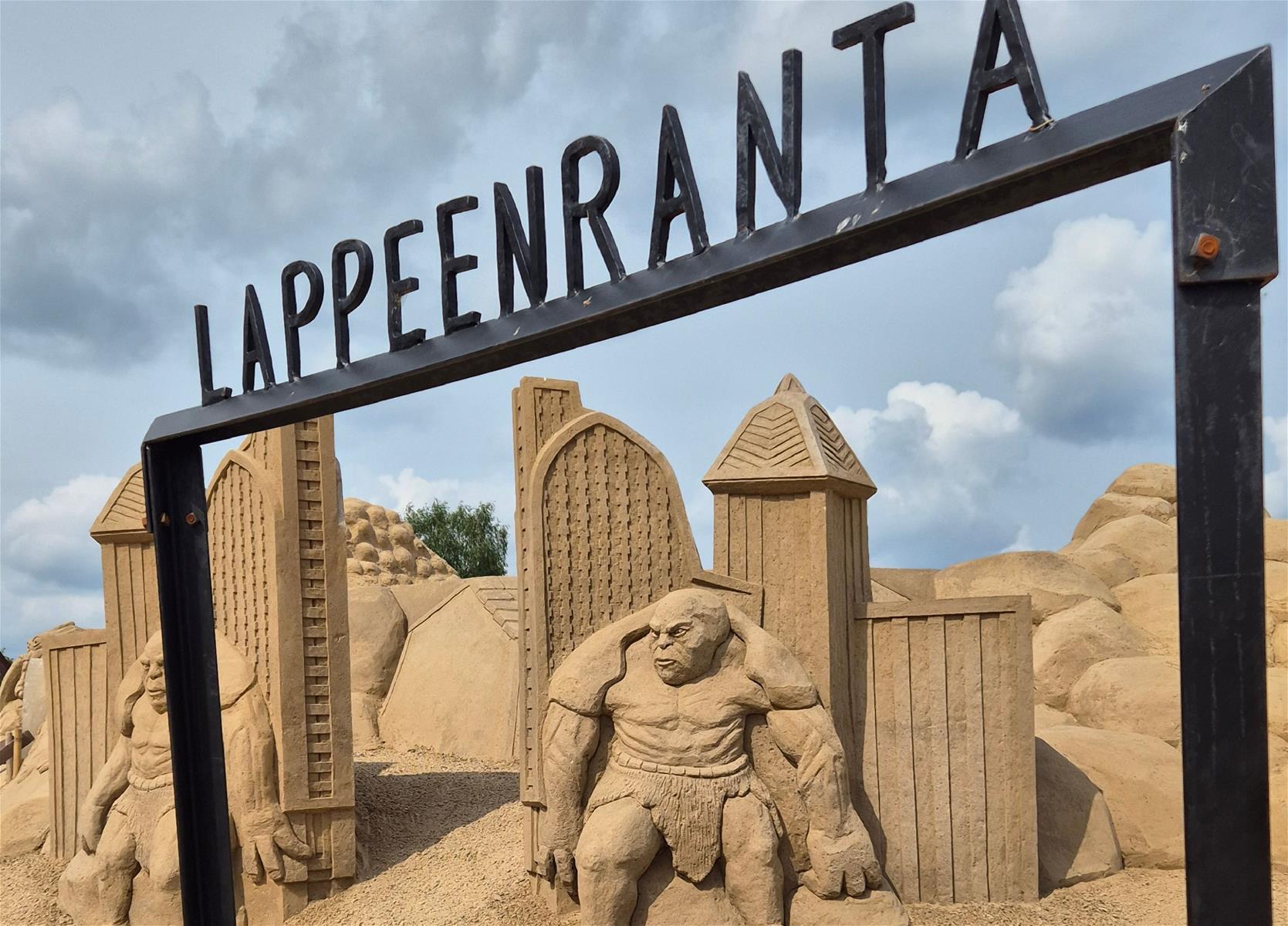 Etualalla rautainen portti, jonka päällä teksti Lappeenranta. Taka-alalla hiekasta muotoiltu linna ja örkkejä.