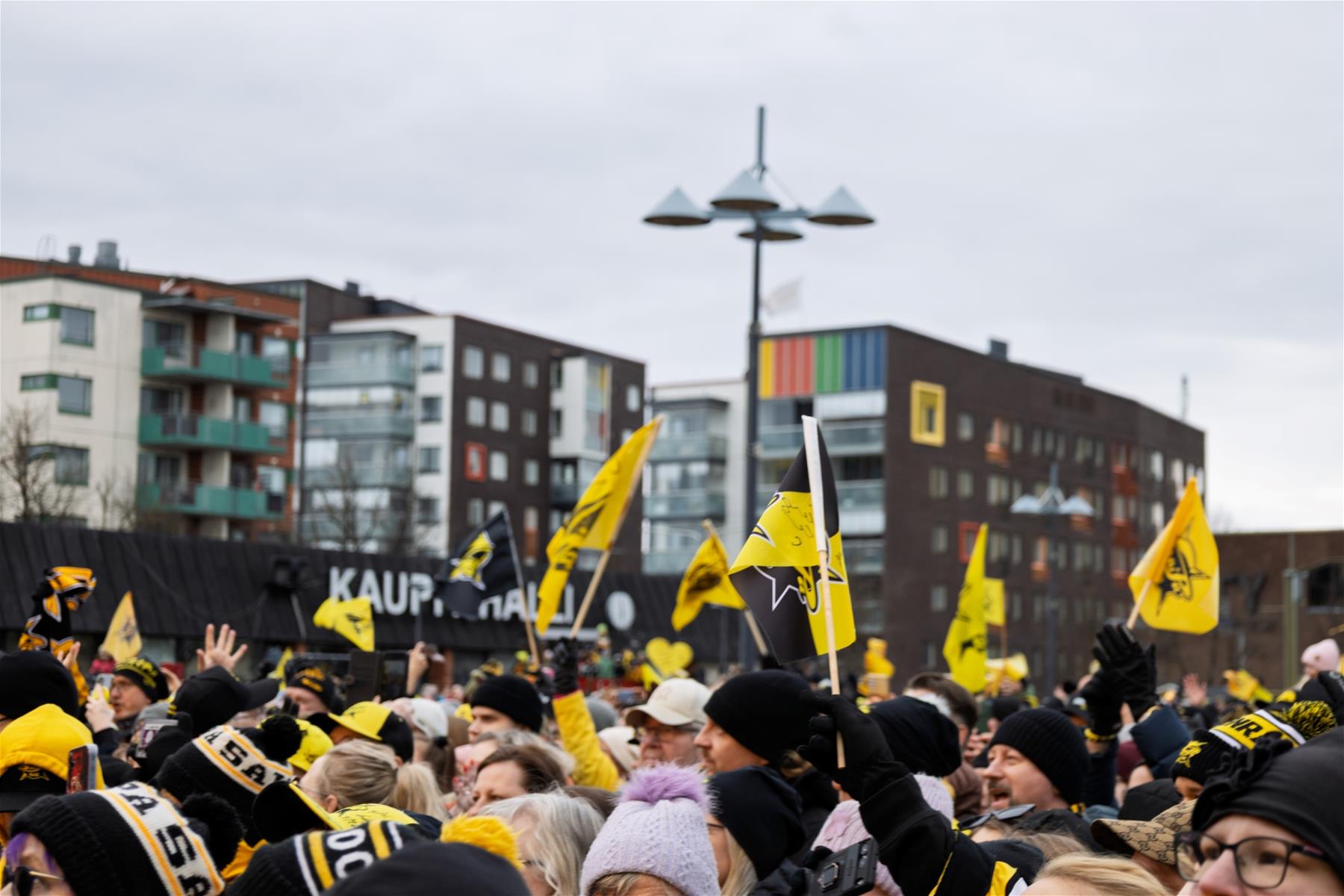 SaiPa-jääkiekkojoukkueen kannatusasuihin pukeutuneita ihmisiä kokoontuneena torille heiluttamaan lippuja. Taustalla kerrostaloja.