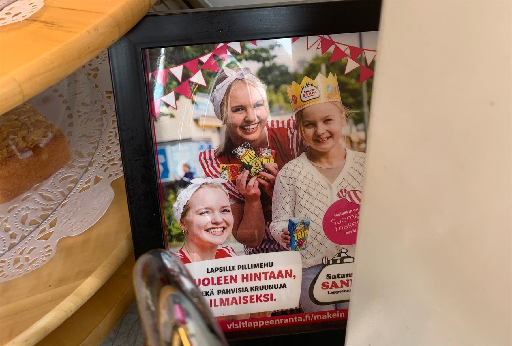 Kuva kehyksissä olevasta mainoksesta, jossa kaksi hymyilevää lasta ja aikuinen.